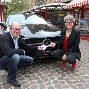 Vor den rot weißen Losbuden steht der schwarze Mercedes, davor hocken links Dietmar Hoppe von der  Bürgerpark-Tombola, rechts Simone Schnase, die Gewinnerin des Mercedes. Symbolisch halten beide einen großen Schlüssel in der Hand. Das Foto wurde von Martin Rospek gemacht.